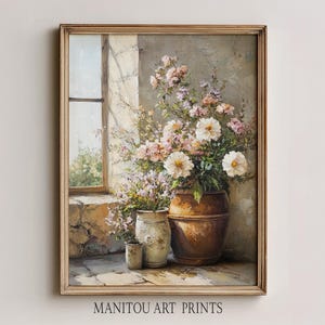 以下が含まれることがあります： 額入りの花の静物画。窓と、白とピンクの花で満たされた3つの花瓶が描かれています。絵画は素朴でヴィンテージな美学を持っています。「MANITOU ART PRINTS」の文字が下にあります。