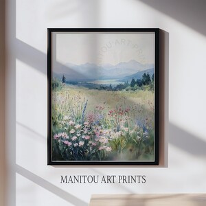 May include: A framed watercolor print of a mountain landscape. The artwork depicts a field of wildflowers in the foreground, with mountains and a valley in the background. The print is framed in a black frame. The text "MANITOU ART PRINTS" is at the bottom.