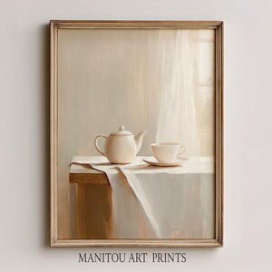 Puede incluir: Pintura enmarcada de naturaleza muerta con una tetera, taza y platillo color crema sobre una mesa cubierta con un paño blanco. La obra de arte tiene una paleta de colores suaves y neutros y una estética vintage. El texto "MANITOU ART PRINTS" está en la parte inferior.