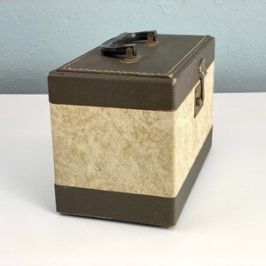 May include: A brown and beige vintage storage box with a black handle and a brass latch. The box has a textured fabric exterior.
