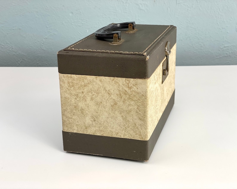 May include: A brown and beige vintage storage box with a black handle and a brass latch. The box has a textured fabric exterior.