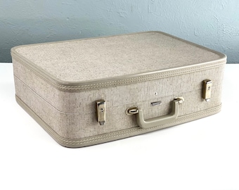 May include: A beige suitcase with a fabric texture and a brown leather trim. It has a metal handle and two metal clasps on the side.