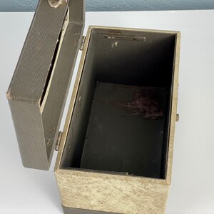 May include: A vintage, gray and beige cardboard box with a hinged lid. The box has a worn, textured surface and a metal latch.