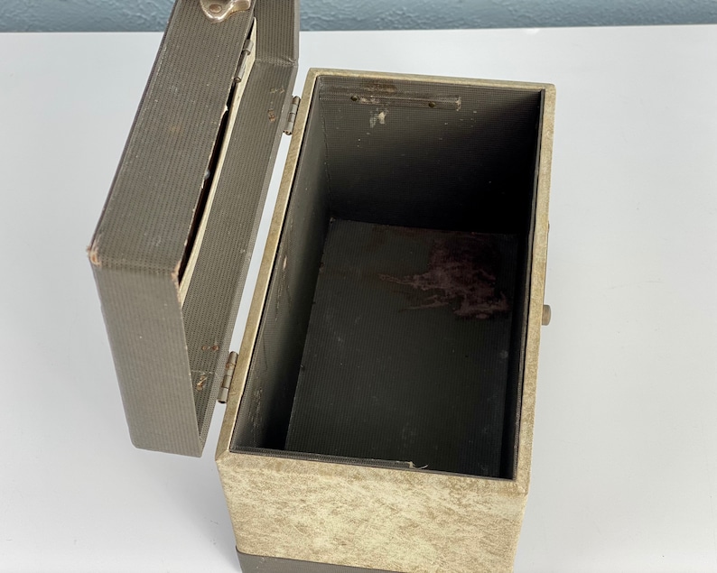 May include: A vintage, gray and beige cardboard box with a hinged lid. The box has a worn, textured surface and a metal latch.