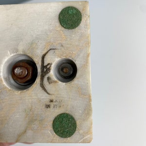 May include: Close-up of the bottom of a white marble sculpture. The sculpture has three metal bolts and two green felt pads on the bottom. The sculpture is marked "MADE IN ITALY".