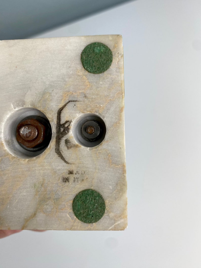 May include: Close-up of the bottom of a white marble sculpture. The sculpture has three metal bolts and two green felt pads on the bottom. The sculpture is marked "MADE IN ITALY".