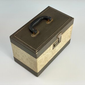 May include: A brown and cream vintage storage box with a black handle and a metal latch. The box has a textured surface and a stitched border.