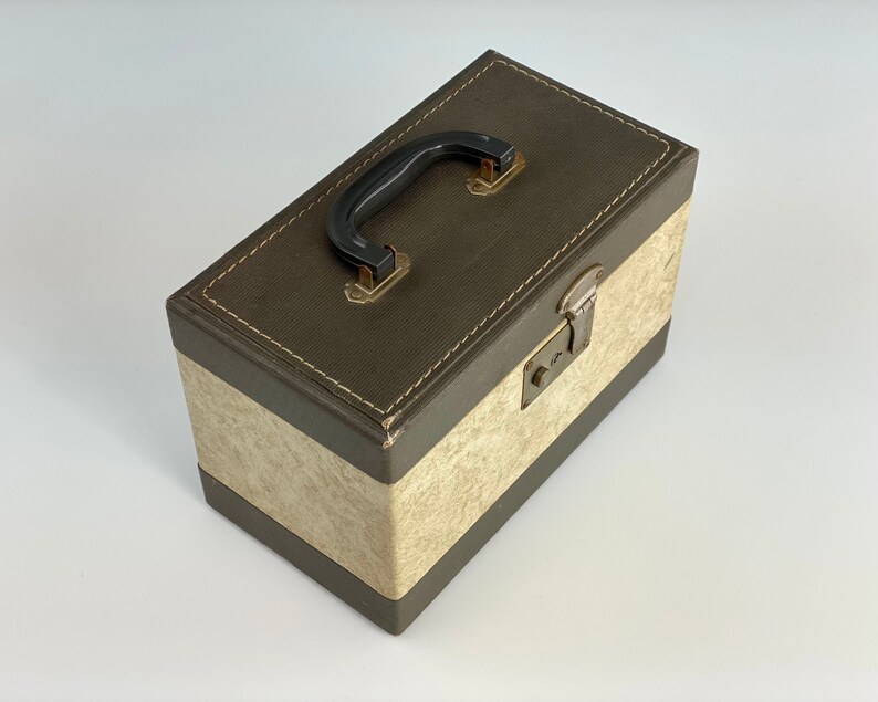 May include: A brown and cream vintage storage box with a black handle and a metal latch. The box has a textured surface and a stitched border.
