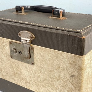 May include: A vintage brown and beige suitcase with a metal latch and a black handle. The suitcase has a textured fabric exterior.
