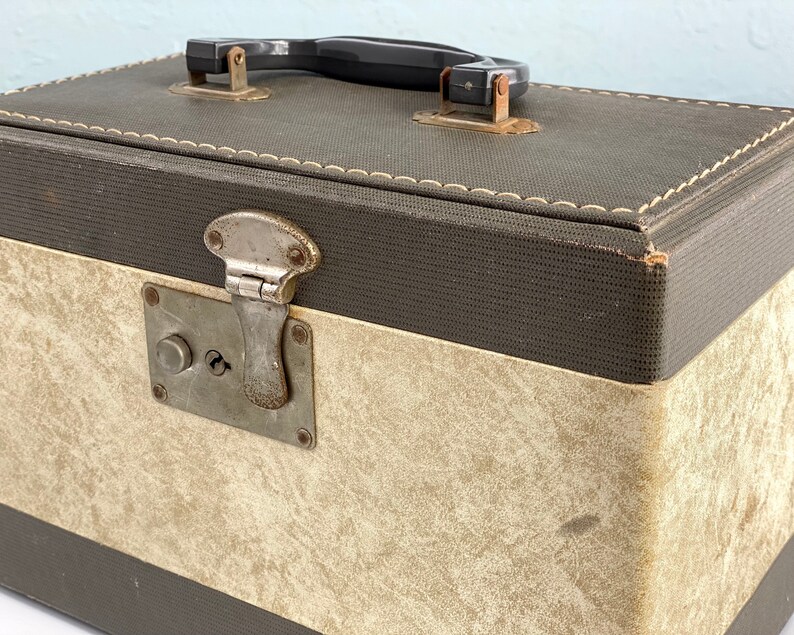May include: A vintage brown and beige suitcase with a metal latch and a black handle. The suitcase has a textured fabric exterior.