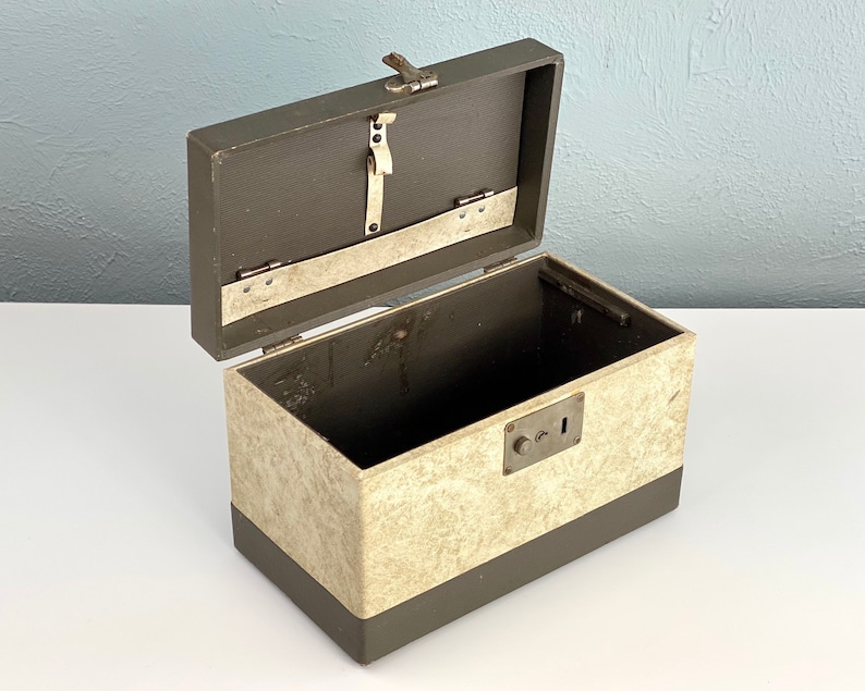 May include: An open vintage metal box with a brown exterior and a cream-colored interior. The box has a lock and a metal latch.
