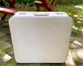 May include: A vintage, light gray suitcase with a textured fabric exterior and a metal handle.