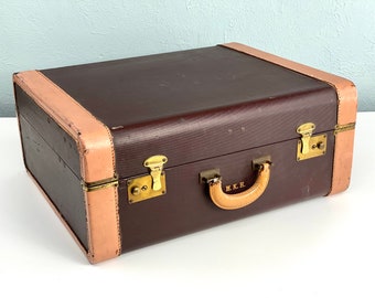 May include: A vintage brown leather suitcase with brass hardware and a tan leather handle. The suitcase has a label that reads "M.K.H."