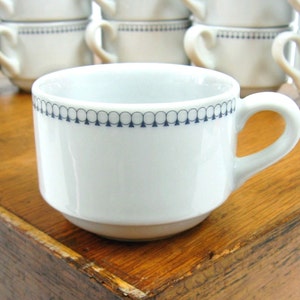 May include: A white ceramic coffee cup with a black and blue trim around the top. The cup has a simple design and is perfect for everyday use.