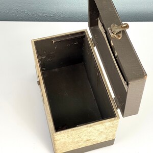 May include: An open vintage storage box with a beige and brown exterior. The box has a hinged lid with a metal latch. The interior of the box is lined with a dark brown material.