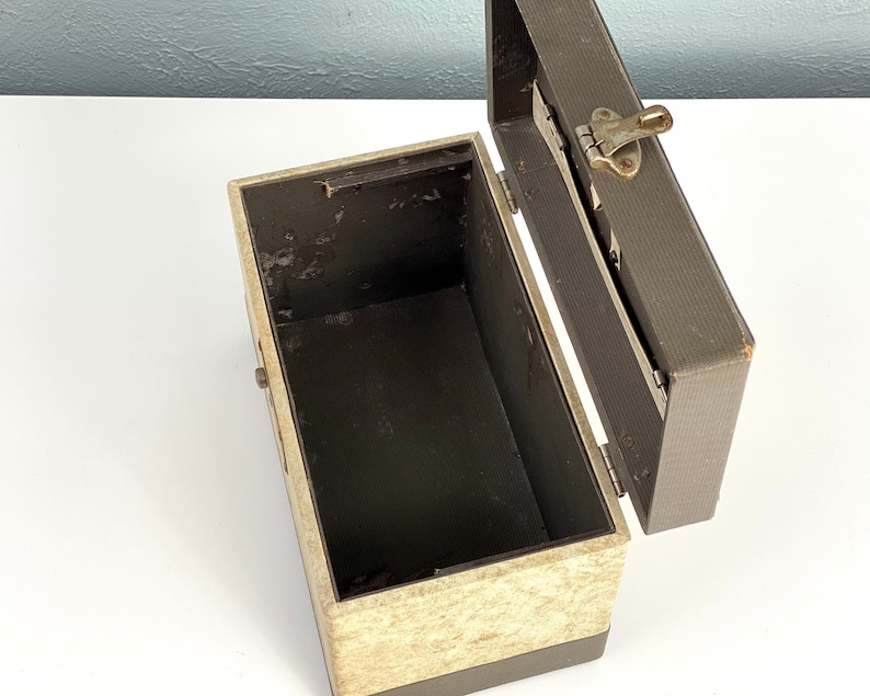 May include: An open vintage storage box with a beige and brown exterior. The box has a hinged lid with a metal latch. The interior of the box is lined with a dark brown material.