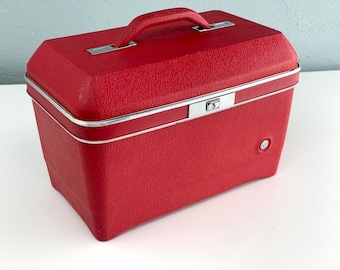 May include: A vintage red travel case with a textured surface, silver trim, and a matching handle. The rectangular case has a secure latch and a small circular button on the side. A classic piece for storage or display.
