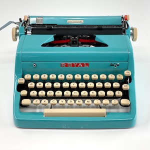 Puede incluir: Una máquina de escribir Royal Quiet De Luxe vintage azul con un teclado de color crema y un logotipo rojo. La máquina de escribir tiene una palanca de retorno de carro y una tecla de tabulación.