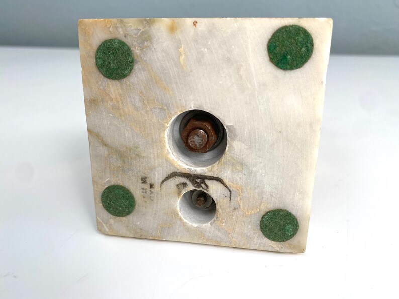 May include: The bottom of a white marble sculpture base with four green felt pads and two metal screws.