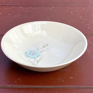 May include: A white ceramic bowl with a blue and green floral design. The bowl is round and has a slightly flared rim.