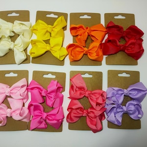 May include: A selection of colourful hair bows in shades of yellow, orange, red, pink, and purple. Each set of bows is attached to a brown card backing, ideal for hair accessories.