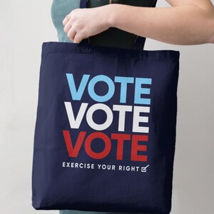 Puede incluir: Una bolsa de tela azul marino con las palabras "VOTE VOTE VOTE" en rojo, blanco y azul. El texto "EXERCISE YOUR RIGHT" está impreso debajo de la palabra "VOTE" en blanco con una marca de verificación.