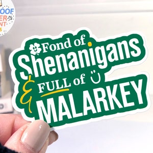 以下が含まれることがあります： 緑と黄色のステッカーに「Fond of Shenanigans & Full of Malarkey」の文字が書かれています。