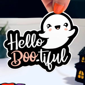 以下が含まれることがあります： かわいい幽霊と「Hello Boo-tiful」というテキストが書かれた、黒と白のハロウィーンステッカーです。