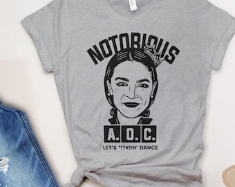 May include: Gray t-shirt with a black graphic of a woman with a crown and the text "NOTORIOUS A.O.C. LET'S "!"#"IN' DANCE"