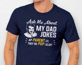 May include: Navy blue t-shirt with a white cartoon illustration of a man with the text "Ask Me About My Dad Jokes AP-PARENT-LY, THEY'RE POP-ULAR!"