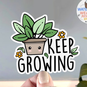 May include: A white sticker with a green plant in a brown pot with a cute face. The text "KEEP GROWING" is in black letters.