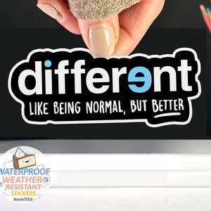 May include: A black and white sticker with the text "different" in white with a blue dot above the "e". The text "LIKE BEING NORMAL, BUT BETTER" is written in white below the word "different".