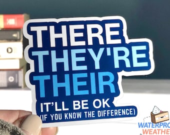 Op de afbeelding: Een blauwe en witte sticker met de woorden "THERE THEY'RE THEIR IT'LL BE OK IF YOU KNOW THE DIFFERENCE)" erop gedrukt. De sticker is waterdicht en weerbestendig.