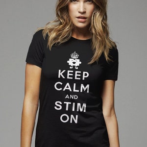 Puede incluir: Camiseta negra con un gráfico blanco que dice "Keep Calm and Stim On" con una pieza de rompecabezas sonriente que lleva una corona sobre el texto.