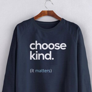 以下が含まれることがあります： 白で「choose kind. (it matters)」とプリントされたネイビーブルーのスウェットシャツ
