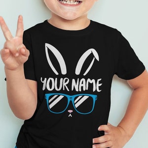 May include: A black t-shirt with a white bunny rabbit graphic wearing blue sunglasses. The text "YOUR NAME" is printed below the graphic.