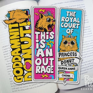 Puede incluir: Tres marcap&aacute;ginas coloridos con ilustraciones de gatos y texto llamativo. Uno de los marcap&aacute;ginas dice "GODDAMNIT DONUT!" en amarillo y negro. Otro dice "THIS IS AN OUTRAGE" en rosa y blanco. El tercero dice "THE ROYAL COURT OF PRINCESS DONUT THE QUEEN ANNE CHONK".