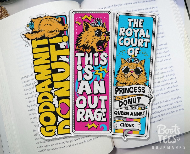 Puede incluir: Tres marcap&aacute;ginas coloridos con ilustraciones de gatos y texto llamativo. Uno de los marcap&aacute;ginas dice "GODDAMNIT DONUT!" en amarillo y negro. Otro dice "THIS IS AN OUTRAGE" en rosa y blanco. El tercero dice "THE ROYAL COURT OF PRINCESS DONUT THE QUEEN ANNE CHONK".