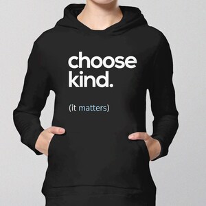 以下が含まれることがあります： 白い文字で「choose kind. (it matters)」と書かれた黒いフード付きスウェットシャツです。