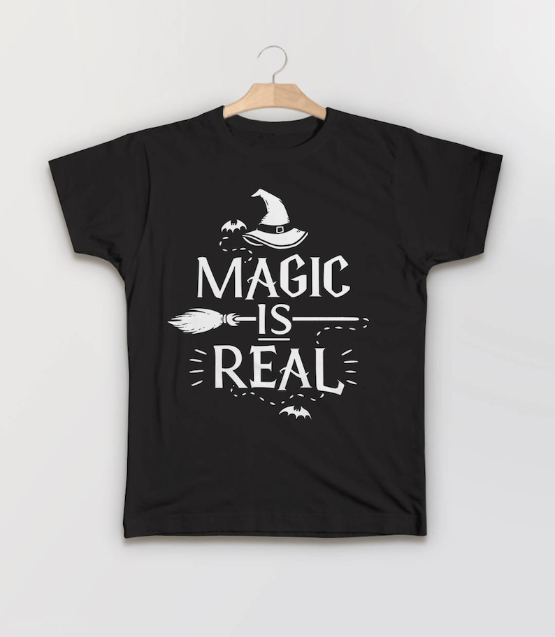 May include: Black t-shirt with a white graphic design featuring a witch's hat, a broom, and the text "Magic is Real".