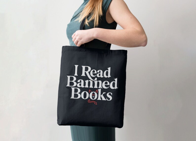May include: A black tote bag with white text that reads "I Read Banned Books" and a small red devil illustration.