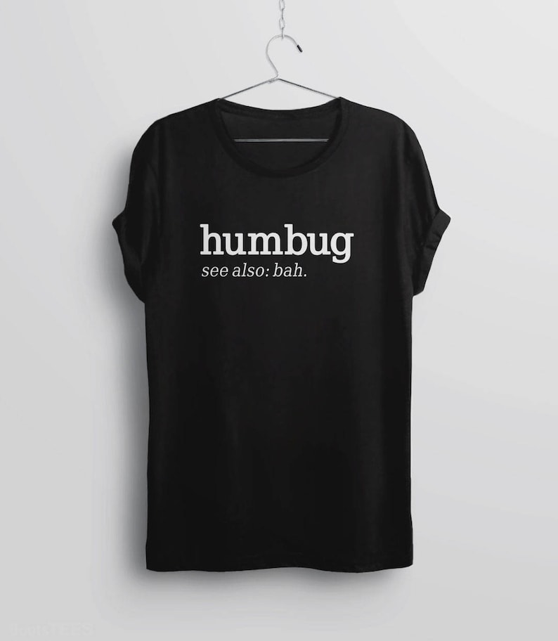 K&ouml;nnte beinhalten: Schwarzes T-Shirt mit dem wei&szlig;en Wort "humbug" und dem Zusatz "see also: bah.". Das T-Shirt h&auml;ngt an einem Metallb&uuml;gel. Die &Auml;rmel des T-Shirts sind hochgekrempelt.