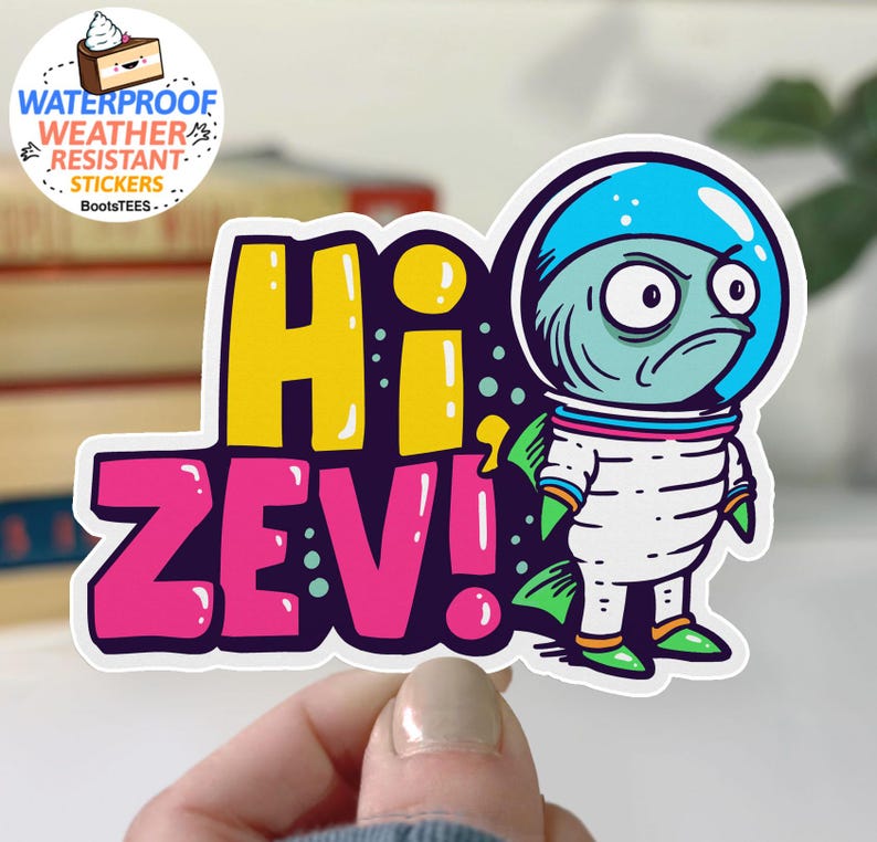 May include: A colorful sticker featuring a cartoon alien astronaut with a grumpy expression. The sticker says "Hi Zev!" in large, bold letters. The sticker is waterproof and weather resistant.