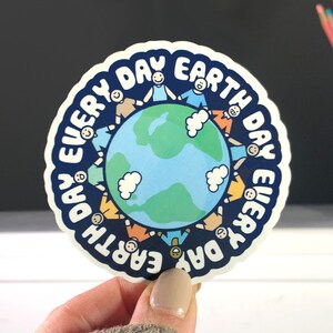 Puede incluir: Una pegatina azul y blanca con el texto "Every Day Earth Day" en un c&iacute;rculo alrededor de una imagen de dibujos animados de la Tierra con personas d&aacute;ndose la mano alrededor.