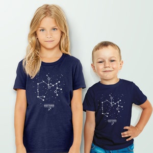 May include: Two children wearing navy blue t-shirts with a white Sagittarius constellation graphic and the text "Sagittarius" printed below. The constellation graphic includes stars and the Sagittarius symbol.