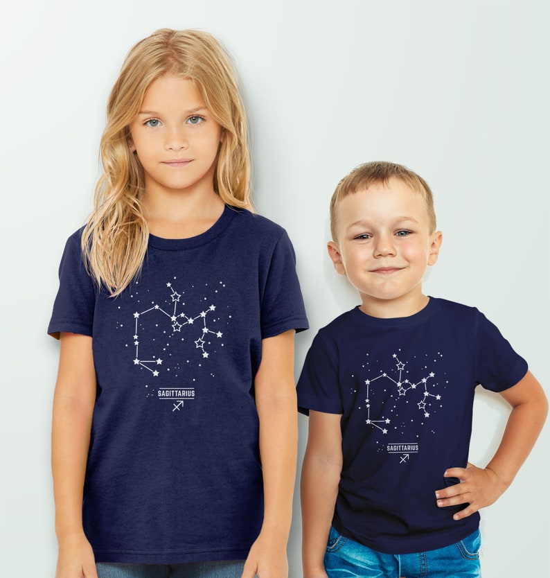 May include: Two children wearing navy blue t-shirts with a white Sagittarius constellation graphic and the text "Sagittarius" printed below. The constellation graphic includes stars and the Sagittarius symbol.