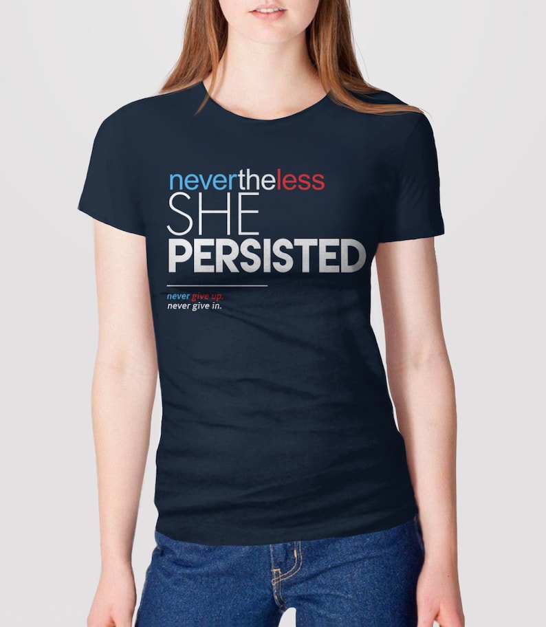 Puede incluir: Una camiseta azul marino con el texto "nevertheless she persisted" en blanco, con las palabras "never" en rojo y "less" en azul. El texto "never give up. never give in." est&aacute; impreso en blanco m&aacute;s peque&ntilde;o debajo del texto principal.