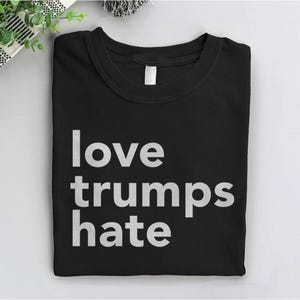 Puede incluir: Camiseta negra con texto blanco que dice "love trumps hate".