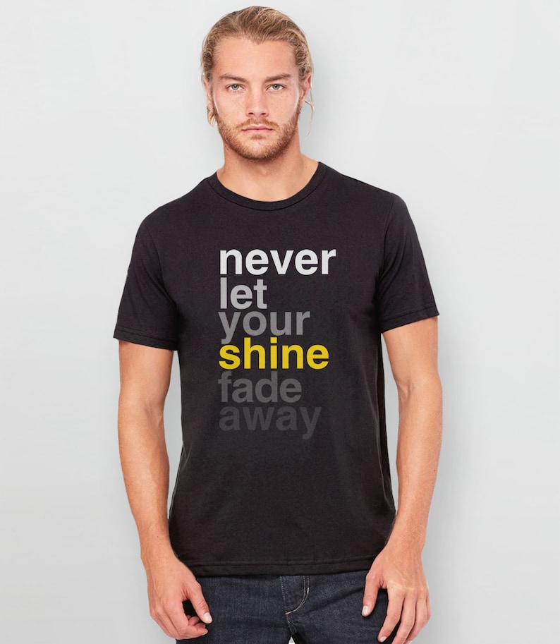 May include: Black t-shirt with a white graphic that reads "never let your shine fade away". The word "shine" is highlighted in yellow.