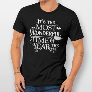 K&ouml;nnte beinhalten: Schwarzes T-Shirt mit wei&szlig;em Text, der "Es ist die sch&ouml;nste Zeit des Jahres" lautet, mit einem Besen, Flederm&auml;usen und Spinnweben.
